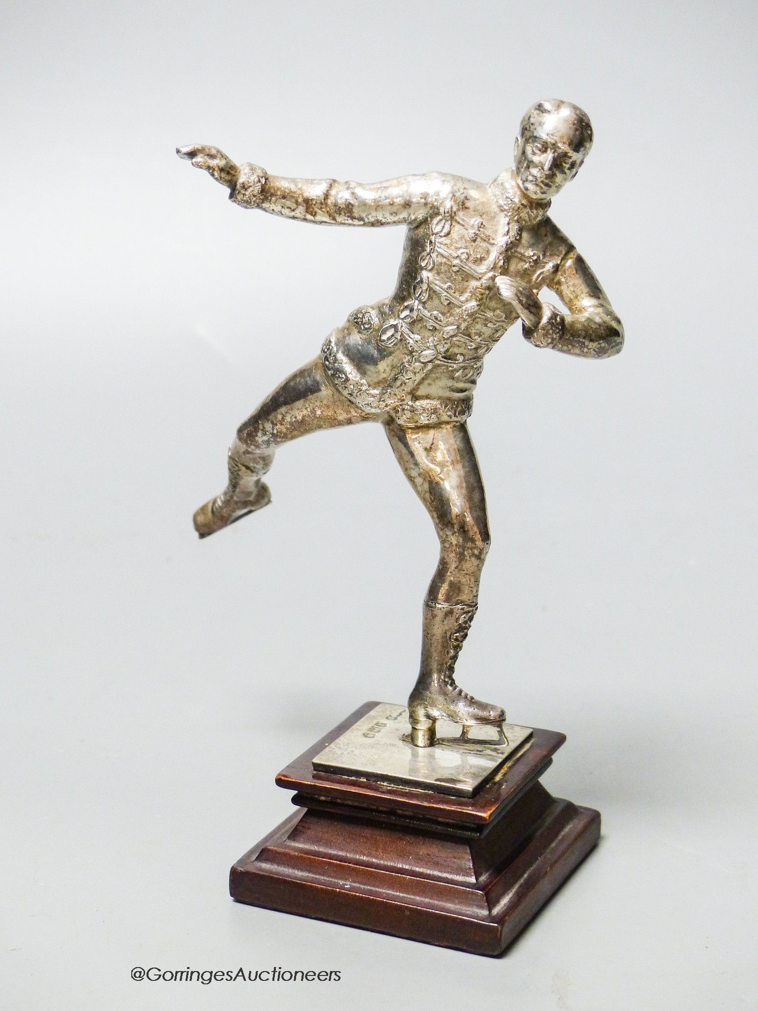 An Edwardian silver miniature model of an ice skater, Elkington & Co Ltd?, London, 1904, on a wooden plinth base, skater 12cm, gross weight 10oz.